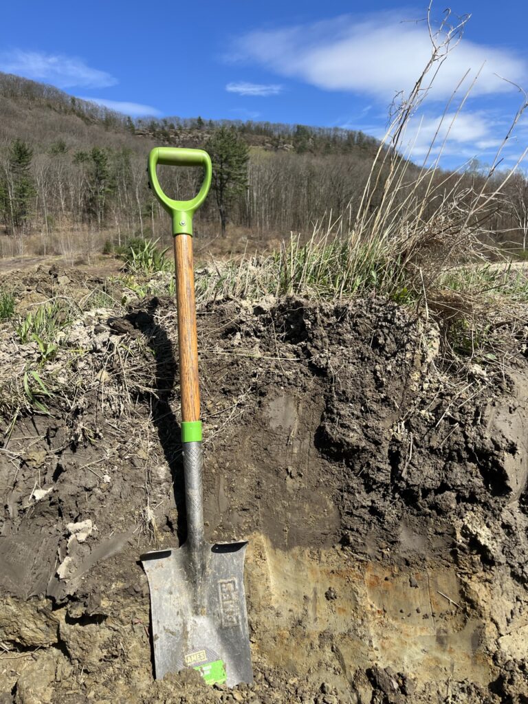 A shovel placed in the dirt on a hillside, highlighting the earthy texture and sloping terrain.